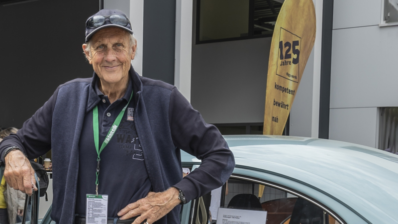 Ein älterer Mann auf dem Außengelände vor der Jubiläumsfahne vom Autohaus