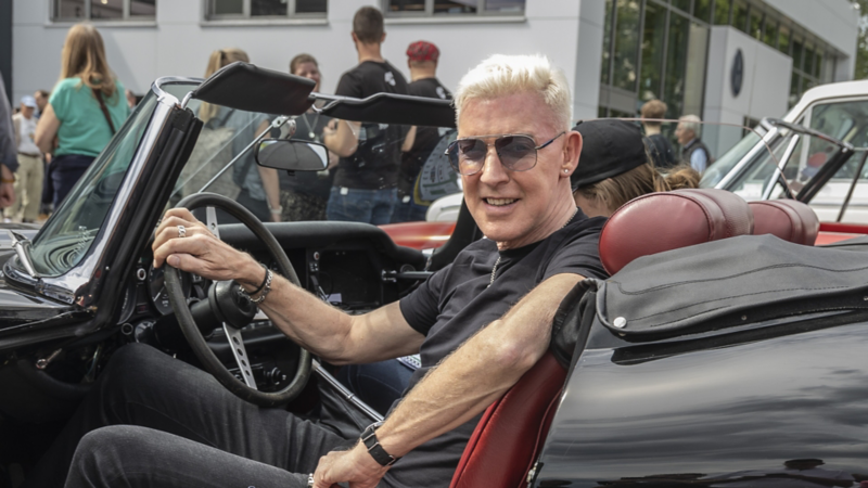 Ein Fahrer im Oldtimer sitzend auf dem Außengelände vom Autohaus