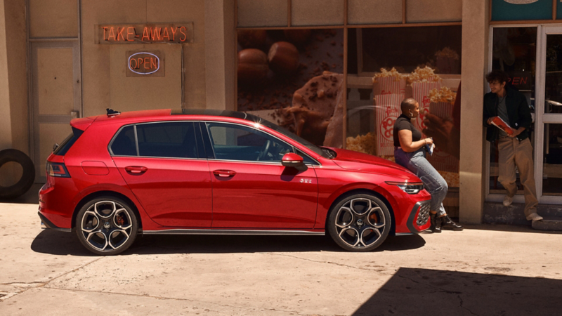 Seitansicht eines roten VW Golf GTI, der vor einem Gebäude steht. 