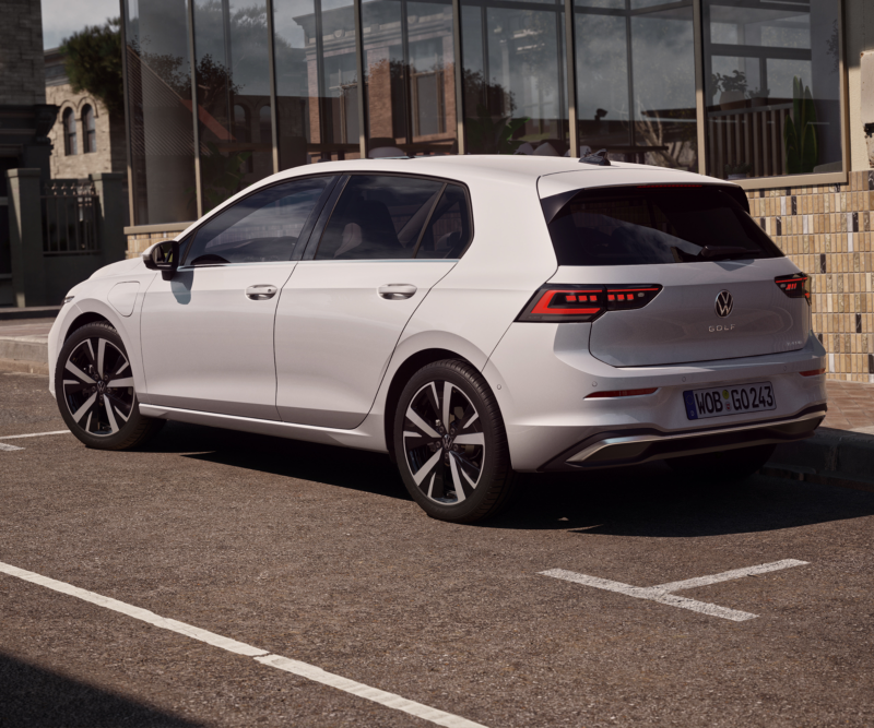 Weißer Volkswagen Golf auf einem Parkplatz vor einem modernen Gebäude.