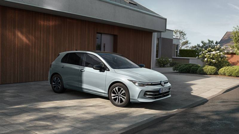 Silberner Volkswagen Golf geparkt vor modernem Haus mit Holzverkleidung, Seiten- und Frontansicht