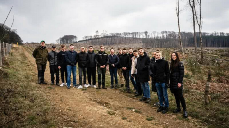Gruppe von 14 Personen steht auf einem Waldweg in einer kargen, winterlichen Landschaft mit kahlen Bäumen im Hintergrund