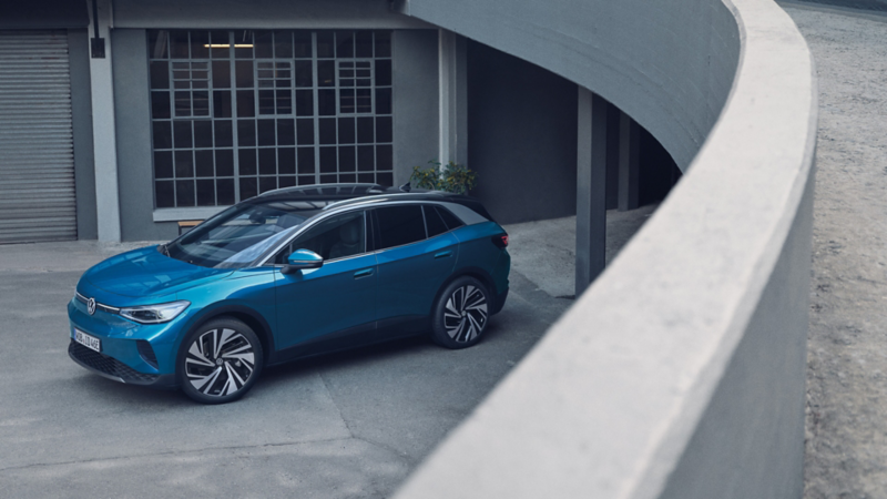 Blauer VW ID.4 parkt seitlich vor einem grauen Gebäudekomplex im modernen Industriestil.