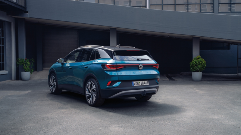 Rückansicht eines blauen VW ID.4, parkt seitlich vor einem grauen Gebäudekomplex im modernen Industriestil.