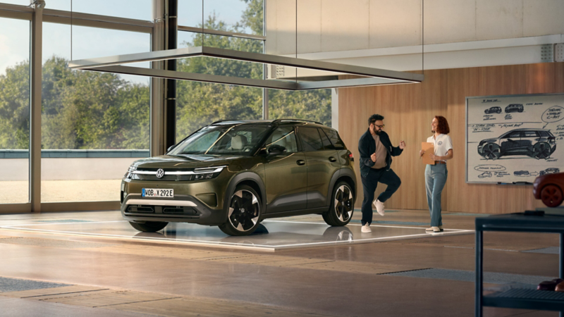 Ein VW ID. Cross steht in einem minimalistisch eingerichteten Designstudio, daneben tänzelt ein aufgeregter Mann und unterhält sich mit einer Ingenieurin.