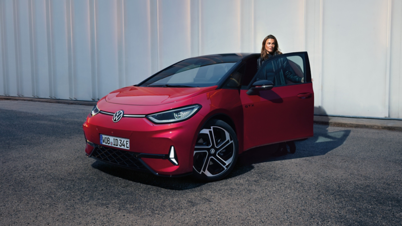 Frontansicht eines VW ID.3 GTX vor einem Gebäude, eine Frau steigt aus der Fahrertür aus.