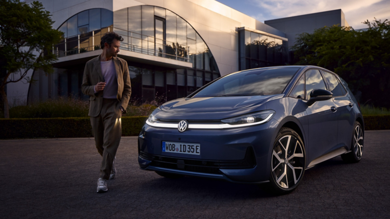 Ein Mann steht vor einem blauen VW ID.3 Neo mit eingeschalteter Lichtanlage und betrachtet die Front des Autos.