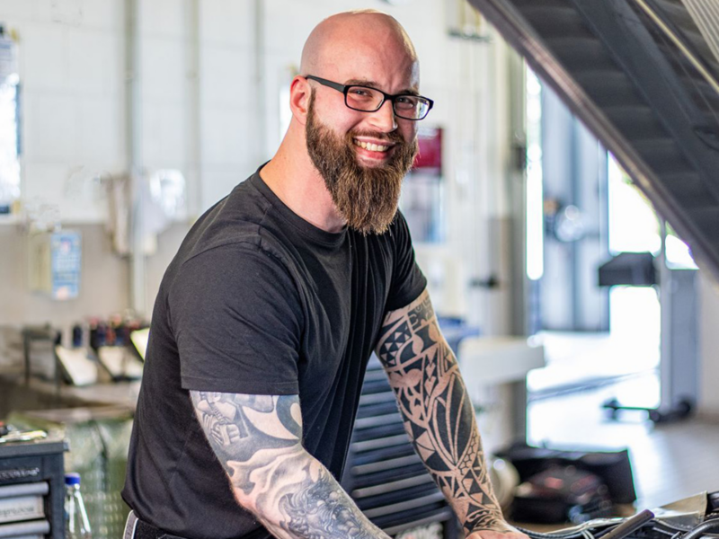Mann mit Bart, Tattoos und Brille läschelt in die Kamera