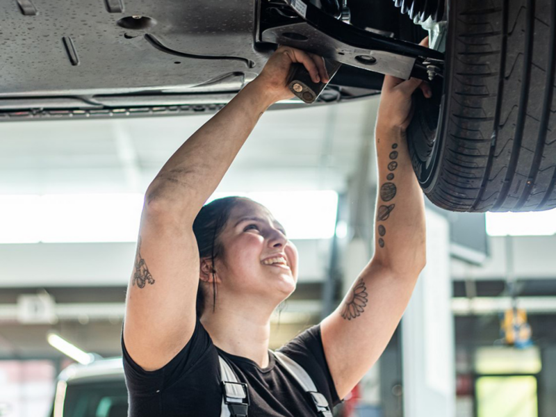 Frau mit Tattoos in Arbeitskleidung schraubt an einem Reifen