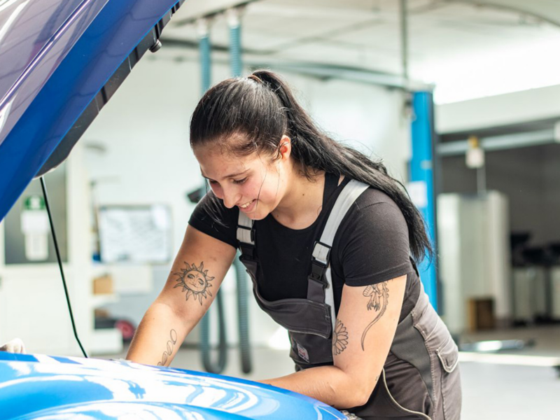 Frau in Arbeitskleidung mit schwarzen langen Haaren in ein Zopf gebunden arbeitet an einem Automotor