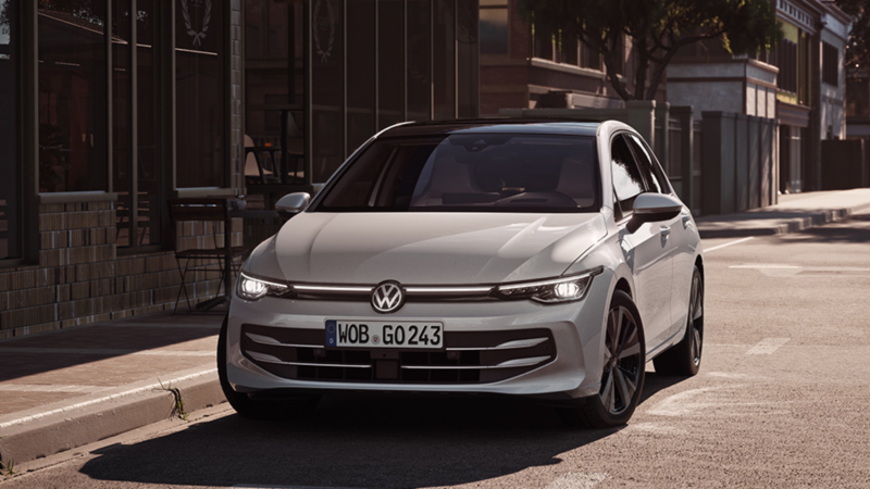 Ein weißer VW Golf parkt am Straßenrand vor einem Café.