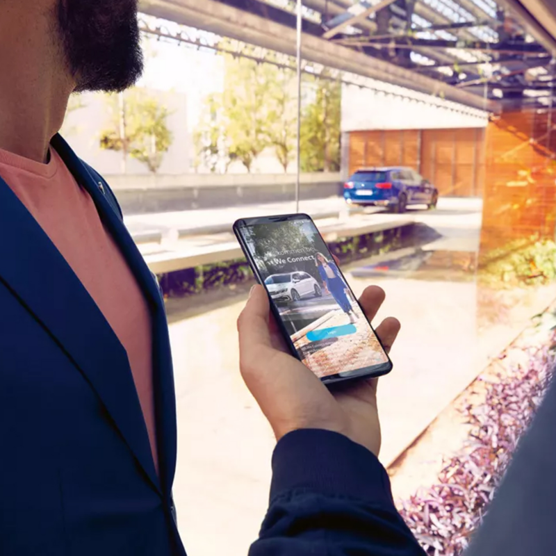 Δύο άνδρες κοιτούν το κινητό τους με ένα μπλέ VW στο βάθος