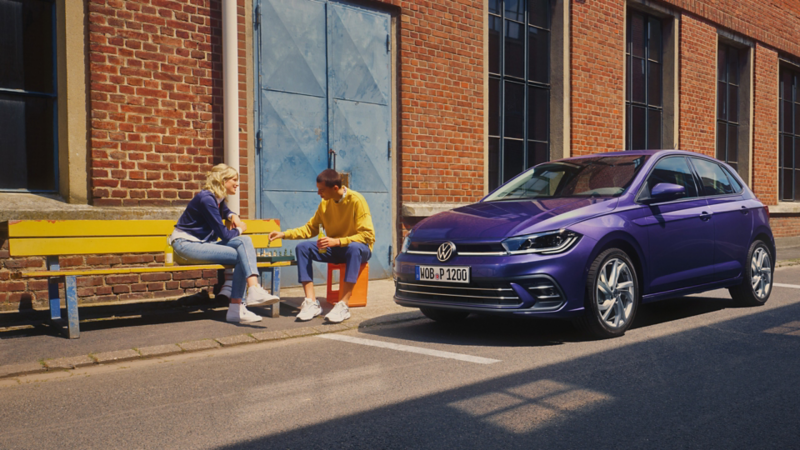 Zwei Personen spielen Schach vor einem roten VW Polo Style, der vor einem Fabrikgebäude parkt.