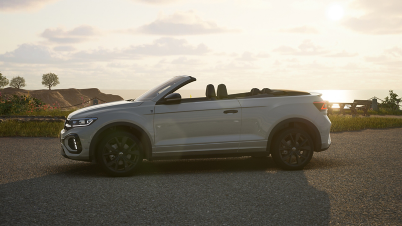 Silbernes Volkswagen T-Roc Cabriolet Edition Karmann mit geöffnetem Verdeck seitlich auf Straße bei Sonnenuntergang