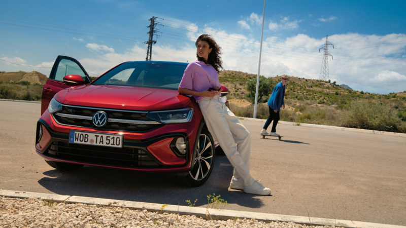 VW Taigo R-Line in Rot, Frontansicht auf Parkplatz. Frau lehnt an Motorhaube, Mann fährt Skateboard.