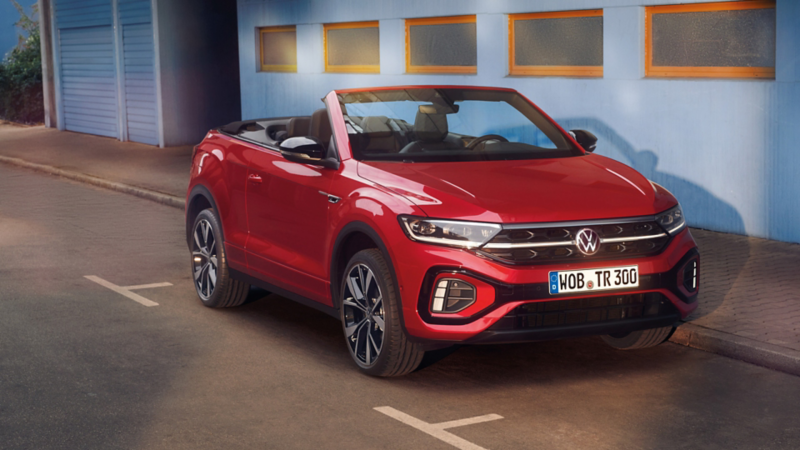 Ansicht der Front eines roten T-Roc Cabriolet mit geöffnetem Dach, parkend am Straßenrand. 