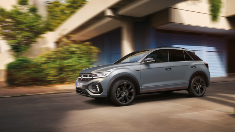 VW T-Roc R-Line in Grau fährt dynamisch über Kreuzung, von der Seite zu sehen