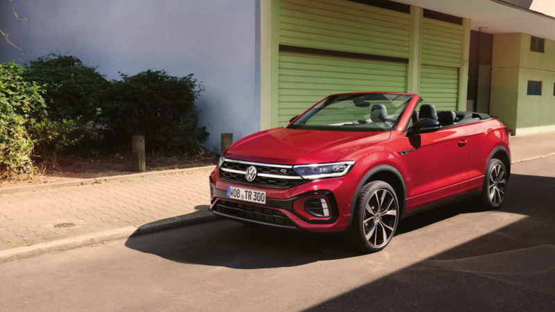 Ein rotes T-Roc Cabriolet parkt am Straßenrand mit geöffnetem Dach.