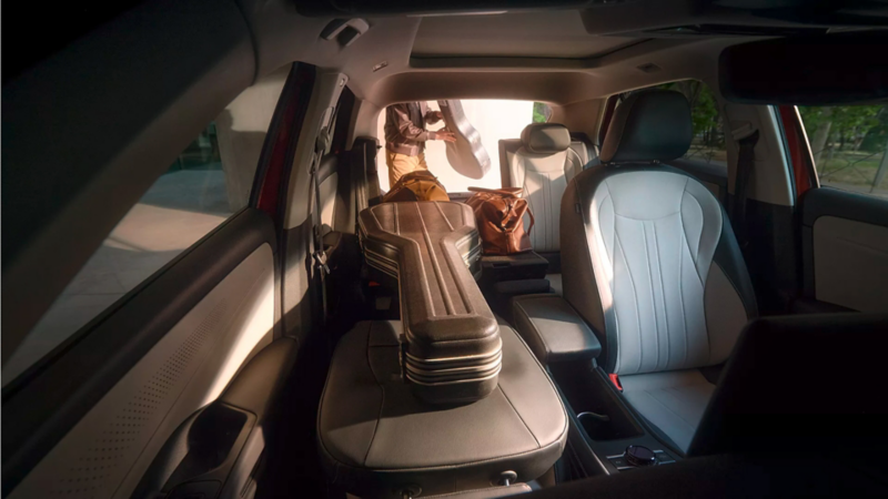 VW T-Roc Innenraum mit umgeklappter Rückbank und vollständig umgeklapptem Beifahrersitz, auf denen ein Gitarrenkoffer liegt.