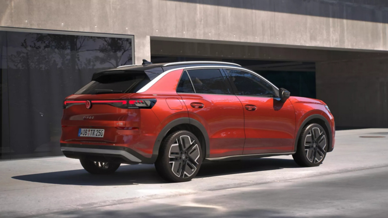 Eine 3/4-Rückansicht eines roten Volkswagen T-Roc Style, parkend vor einem Gebäude. 