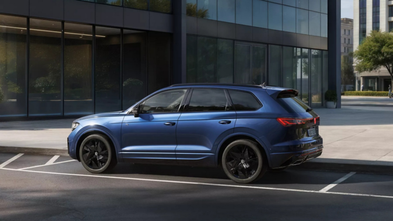 Ein blauer VW Touareg FINAL EDITION steht vor einem Bürogebäude mit Glasfassade - Ansicht von schräg hinten.