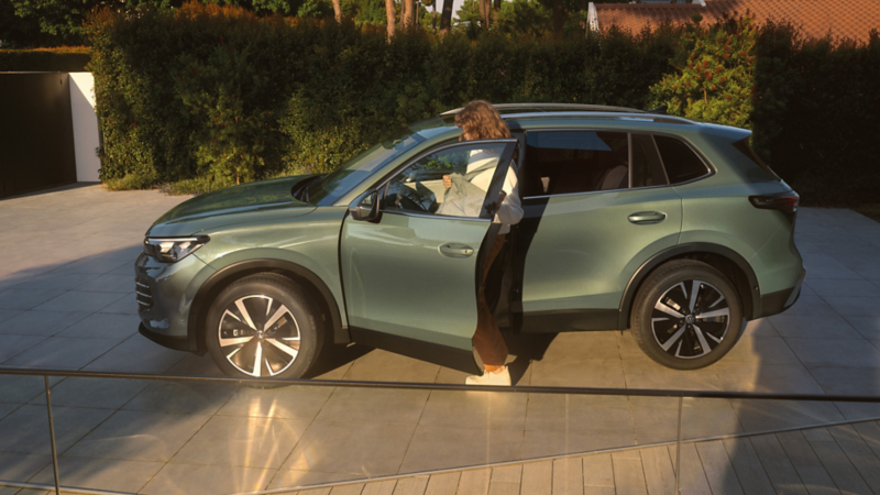 Eine Frau steigt in einen grünen VW Tiguan ein, der auf einer begrünten Auffahrt steht.
