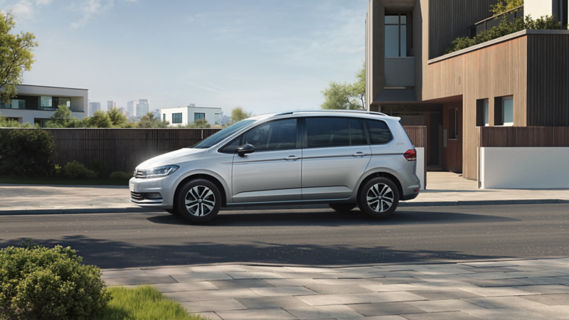 Silberner VW Touran steht seitlich auf einer Straße vor modernen Wohnhäusern bei Tageslicht