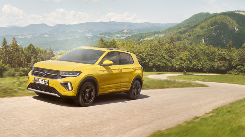 Ein gelber VW T-Cross auf einer Straße in hügeliger Landschaft.