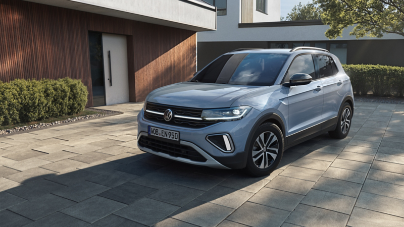 Hellblauer Volkswagen T-Cross SUV steht vor modernem Haus auf gepflasterter Einfahrt