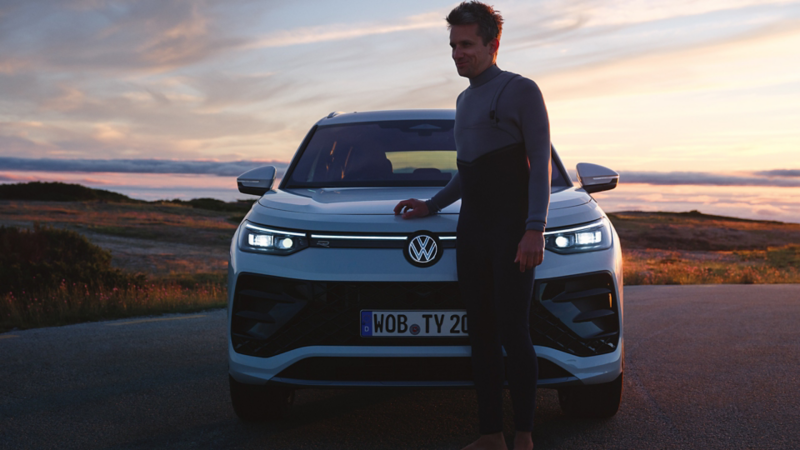 VW Tayron in Weiß auf Parkplatz, Mann steht hinter Auto. Das Meer im Hintergund. 
