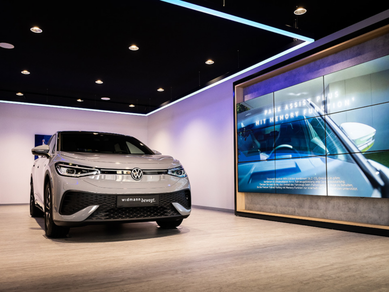 Silberner Volkswagen SUV im Showroom mit moderner Beleuchtung und großem Bildschirm an der Wand
