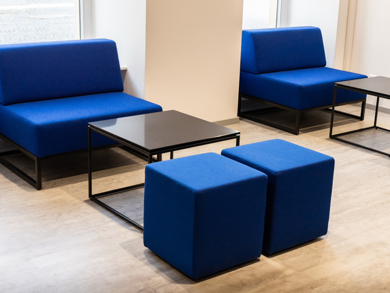 Zwei blaue Sofas und zwei blaue quadratische Hocker um schwarze quadratische Couchtische in einem hellen Raum