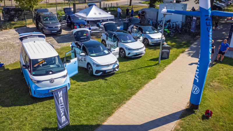 VW Pkw und VW Nutzfahrzeuge stehen nebeneinander im Grünen, draußen an einem hellen, sonnigen Tag