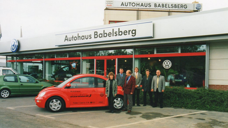 Fünf Personen stehen vor einem roten Volkswagen Beetle vor dem Autohaus Babelsberg mit Volkswagen-Logo
