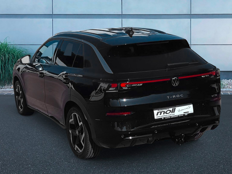 Eine 3/4-Rückansicht eines schwarzen Volkswagen T-Roc R-Line, der vor dem Autohaus Moll in Biberach parkt. 