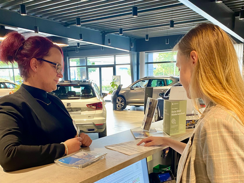 Alina und Kollegin stehen am Empfang des Autohauses und besprechen etwas