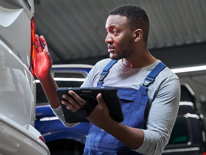 Die Rücklichter eines VW Transporters werden von einem Mechaniker mit Tablet in der Hand geprüft.