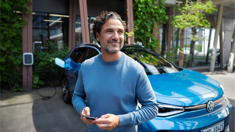 Un hombre de azul sonriendo delaten de un Volkswagen ID.4 conectado a un cargador