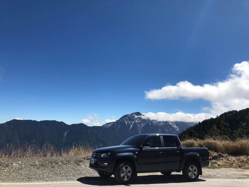 黑色Amarok停在高山路邊，遠方可見山脈及藍天白雲