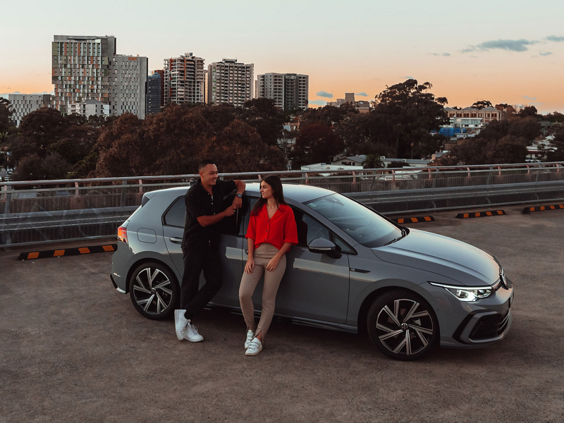 Side angle of the couples beside Volkswagen Golf parked on the roof.