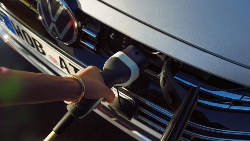 Eine Hand steckt ein Ladekabel in die Ladevorrichtung im Kühlergrill eines VW.