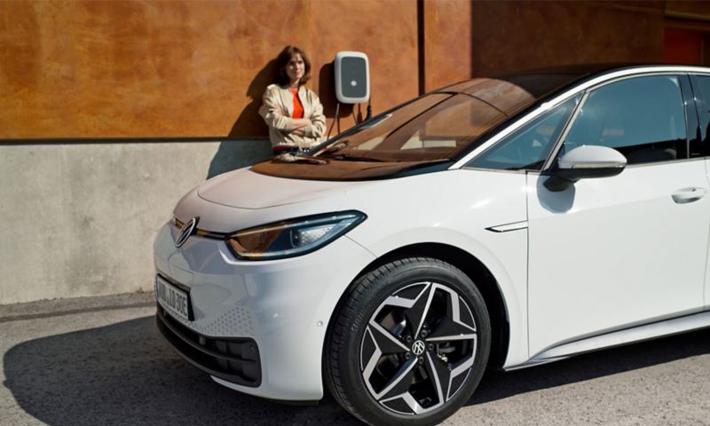 In primo piano la Volkswagen ID.3, dietro la quale una donna sosta accanto alla Wallbox.