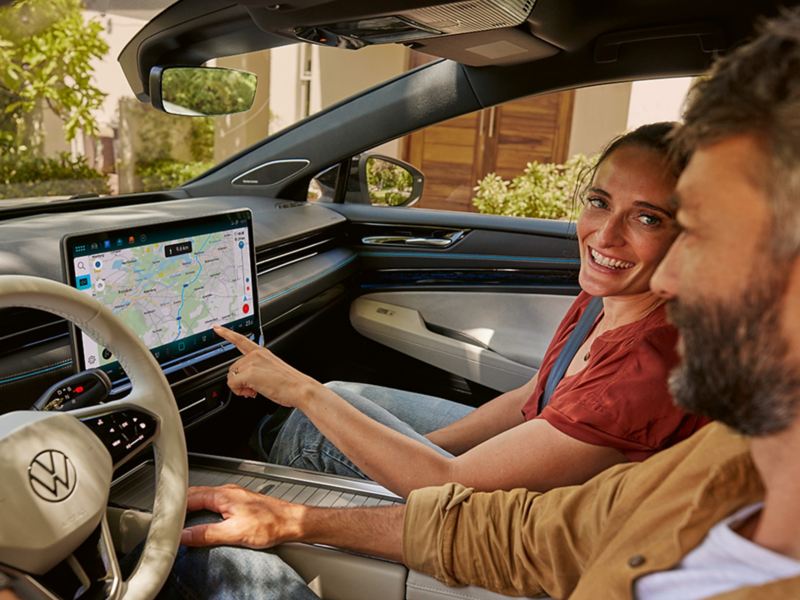 Ein Paar sitzt in einem VW. Die Frau zeigt mit dem Finger auf das Navigationsgerät.