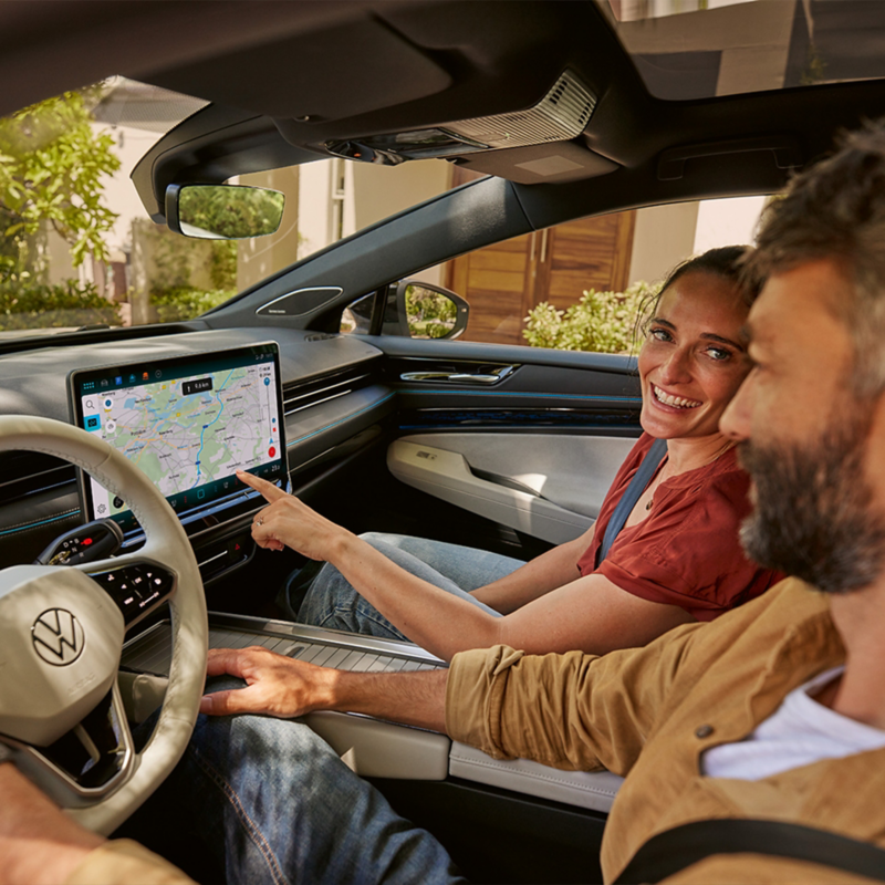 Ein Paar sitzt in einem VW. Die Frau zeigt mit dem Finger auf das Navigationsgerät.