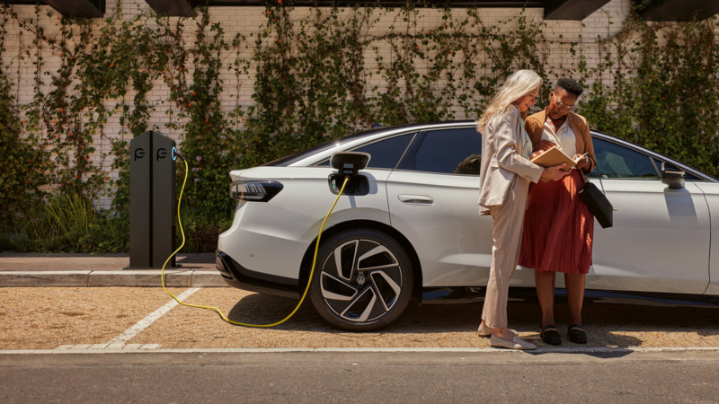 Deux femmes se tiennent devant une voiture électrique en train de se recharger