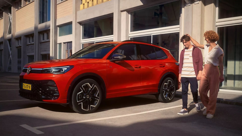 Red VW Tiguan parked in front of a building, a woman and a youth walk next to it.