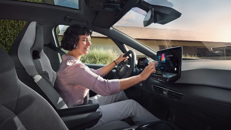 Eine Frau sitzt am Steuer eines VW und gibt mit der Hand etwas auf dem Touchscreen ein.