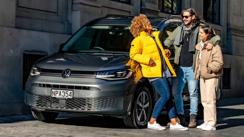 Un grupo de tres personas junto a un VW Caddy gris.
