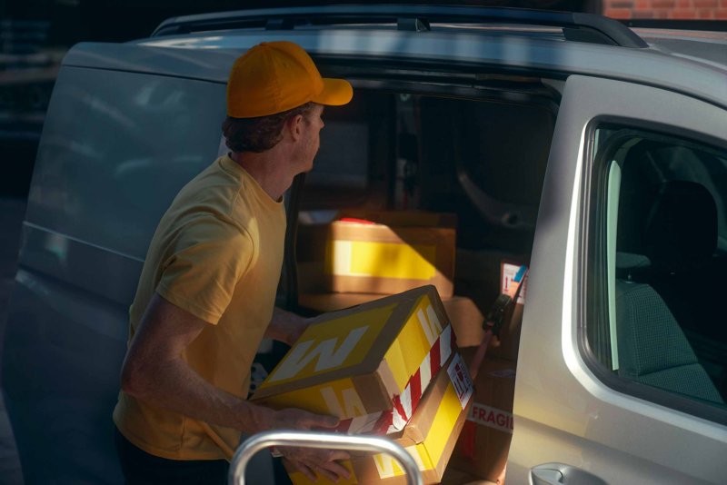 Courier boy loading large boxes into Volkswagen Caddy Cargo through side sliding door.