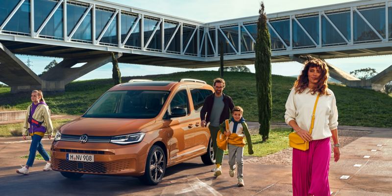 Orange VW Caddy parkeret med en familie på vej ud af den